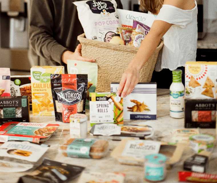 Man and woman standing by a table with lots of vegan snacks and a grocery bag