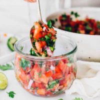 woman filling fresh tomato salsa in a glass jar with a spoon