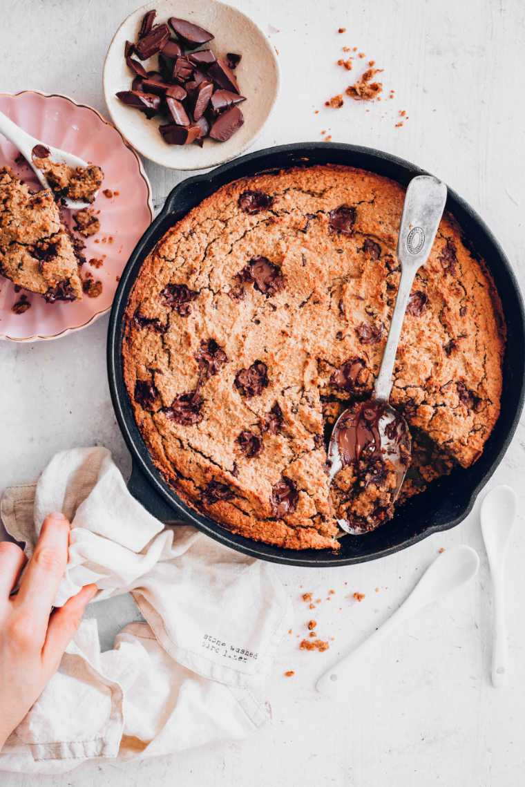 hand holding a towel and cast iron skillet with freshly baked vegan chocolate chip cookie cake