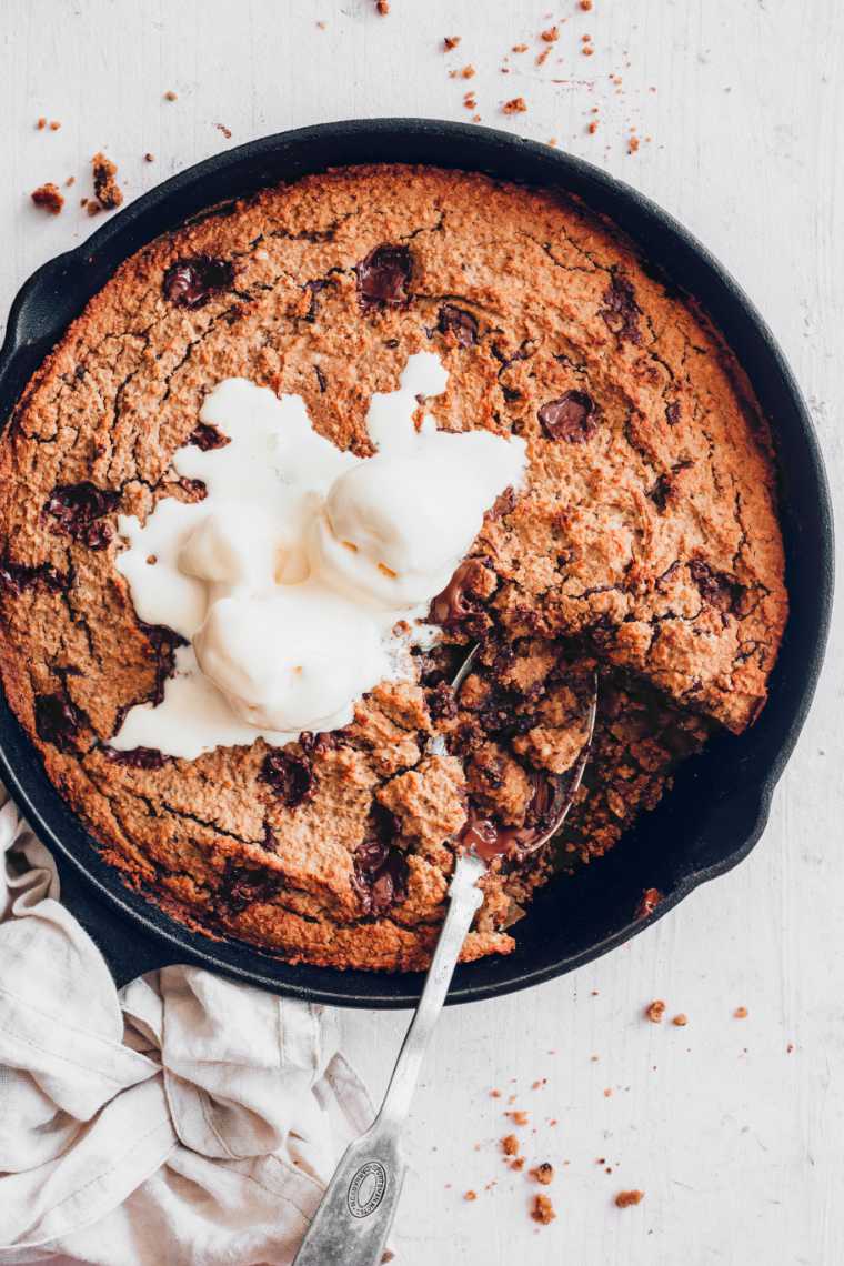cast iron skillet with homemade vegan cookie cake and ice cream on a table with a spoon