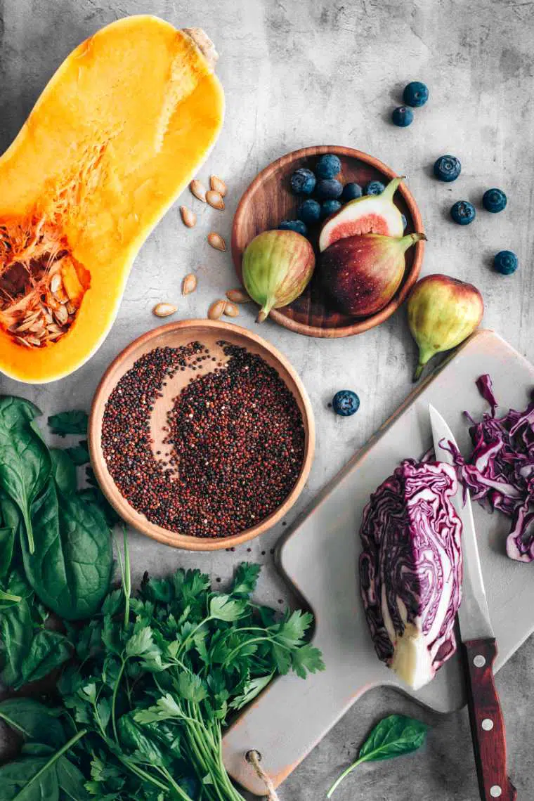 stone surface with a halved butternut squash, fresh figs, blueberries, quinoa, greens and red cabbage