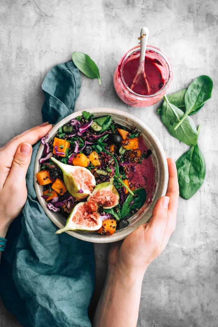 two hands holding a vegan harvest bowl with quinoa, roast pumpkin, spinach, fig and blueberry dressing