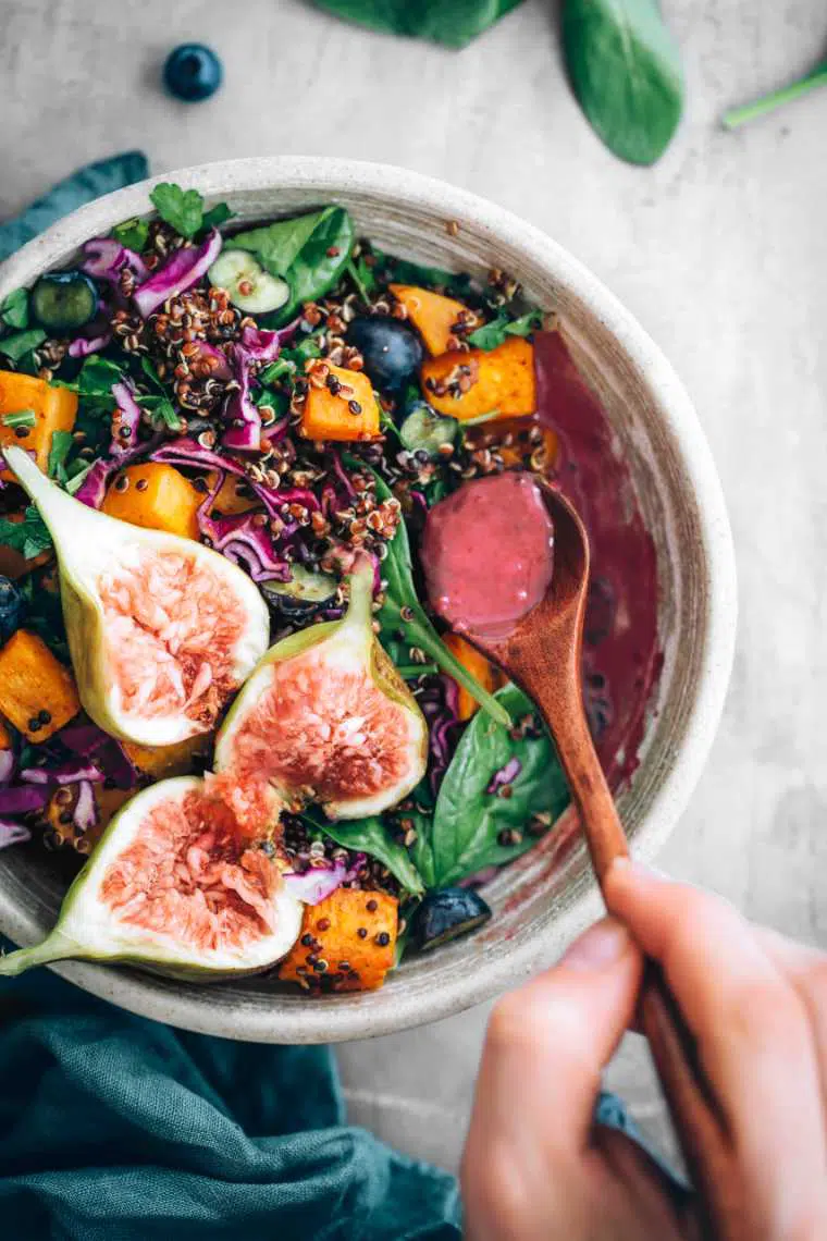 hand drizzling blueberry dressing over vegan harvest bowl with fresh figs and spinach