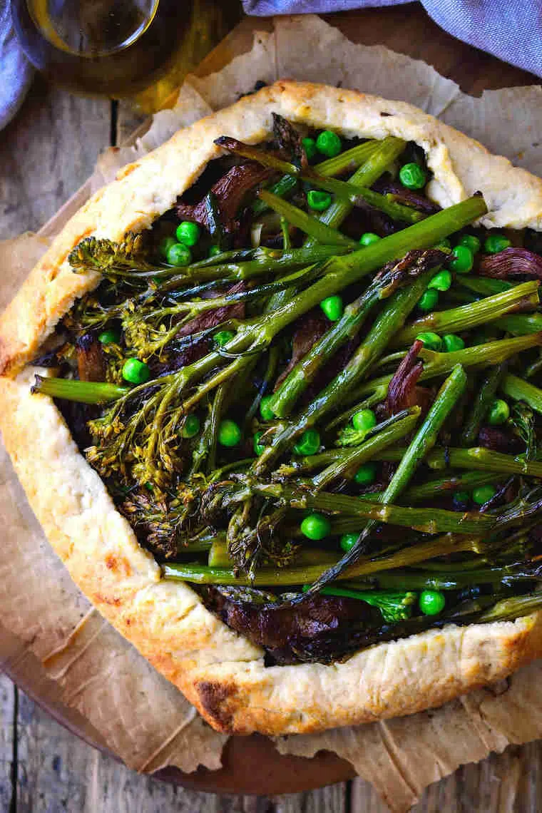 close up of a vegan galette loaded with spring vegetables such as broccoli or asparagus on some parchment paper