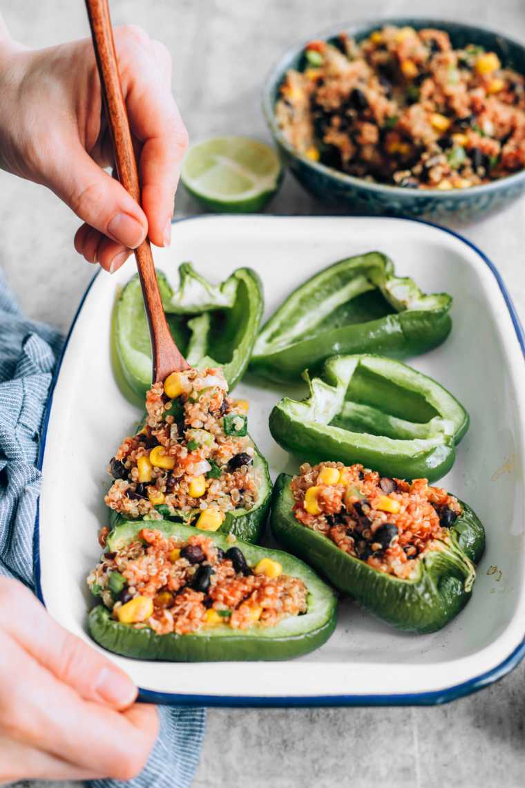 halved bell peppers being stuffed with plant-based gluten-free quinoa mixture