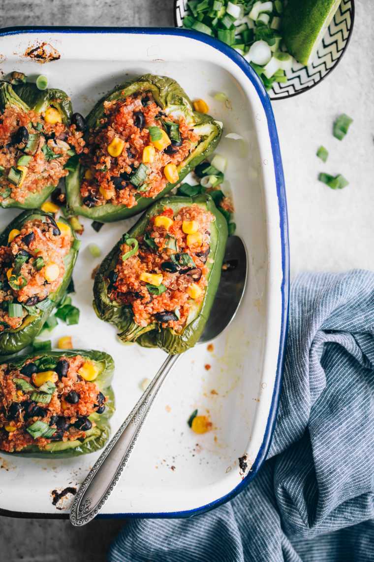 white baking dish on a table with five green plant-based stuffed peppers