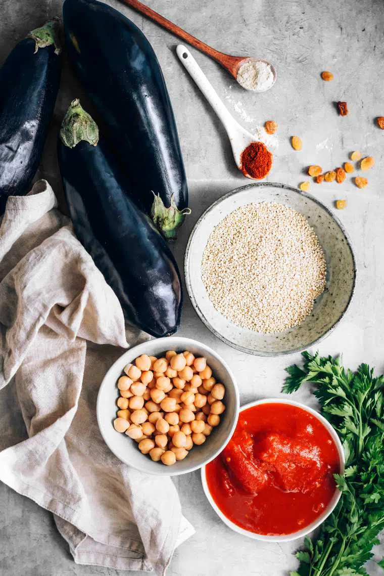 fresh aubergines, uncooked quinoa, chickpeas, tomato sauce and parsley on a table