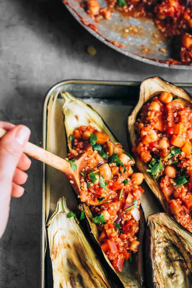 baked aubergines on baking pans being filled with quinoa chickpea mixture