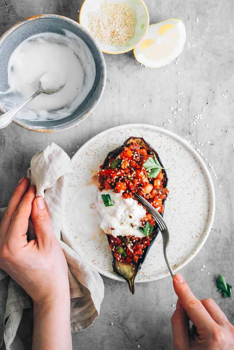 hand holding a white plate and a fork which is cutting into vegan quinoa stuffed aubergine