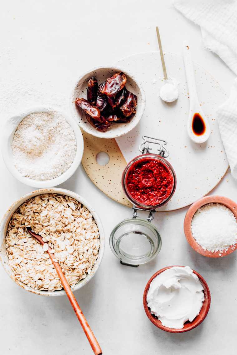 white table with a bowl of rolled oats, flour, dates, coconut cream, chia jam and spices