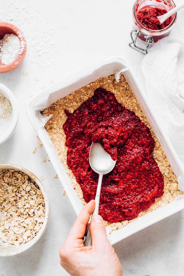 white baking dish with oatmeal flapjack mixture which is being topped with raspberry chia jam