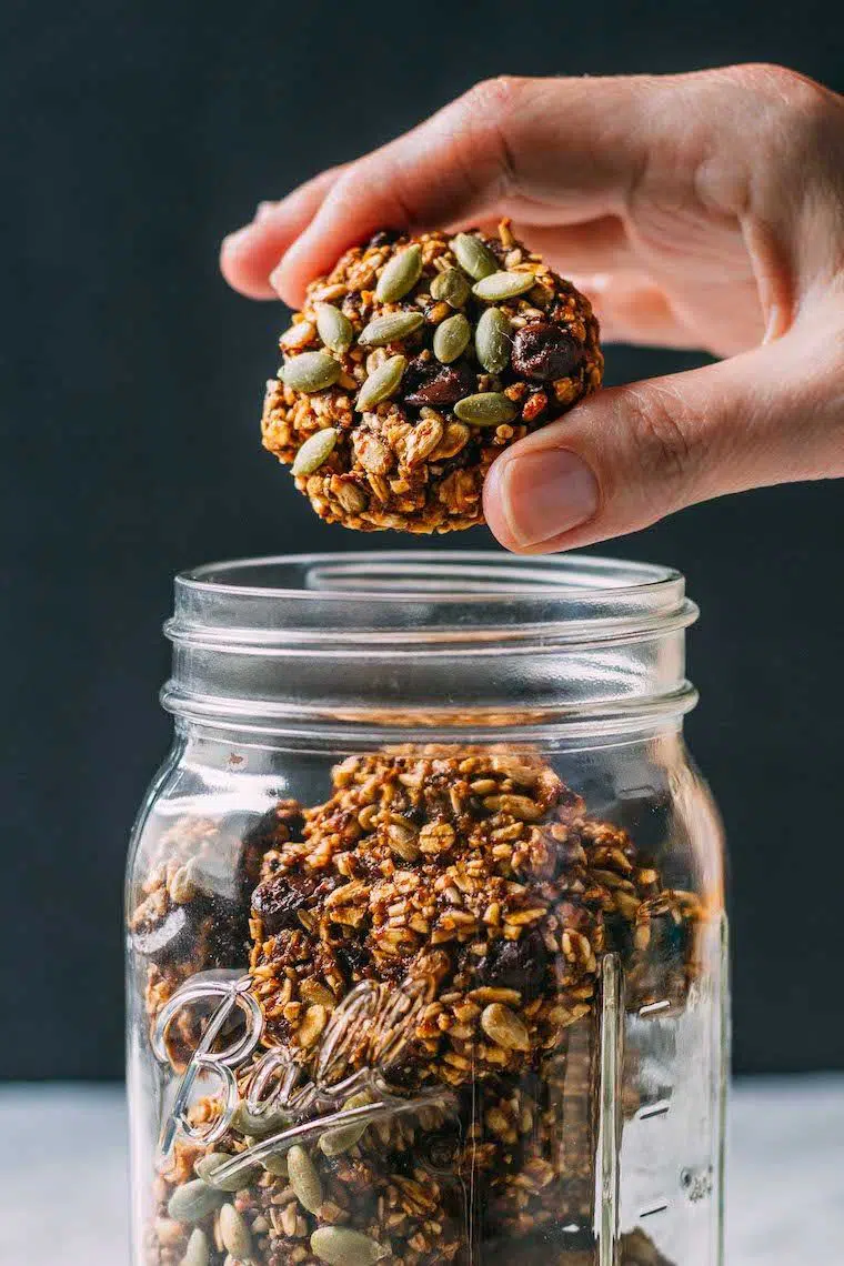 mason jar filled with healthy protein-rich superfood pumpkin cookies, one of which is being taken out by a hand