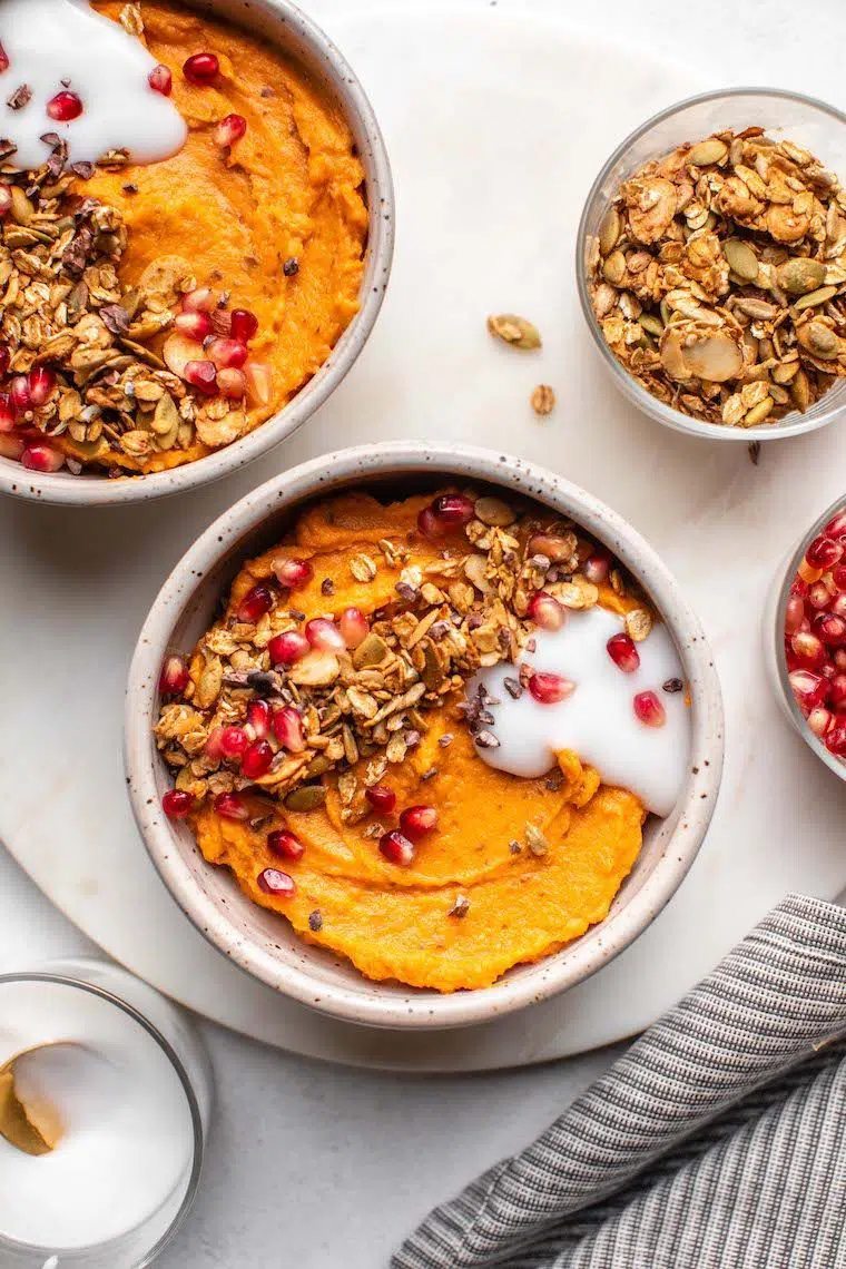 two white bowls with blended orange sweet potato, some granola and vegan yoghurt