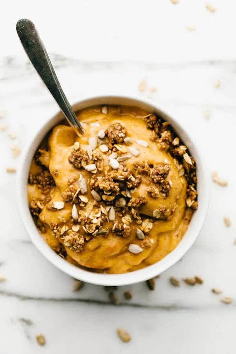 white bowl with yellow sweet potato nice cream topped with granola and sunflower seeds