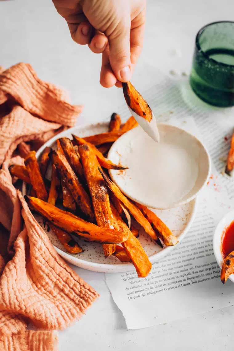 white table with a speckled plate full of oil-free sweet potato fries one of which is being dipped in cashew sour cream