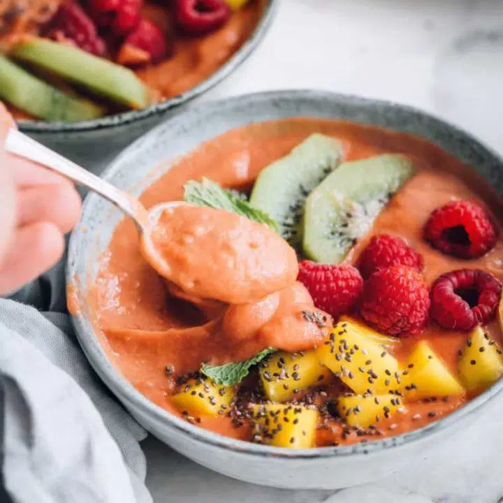 two grey bowls filled with tropical sweet potato smoothie bowl, topped with mango, kiwi, raspberries and mint