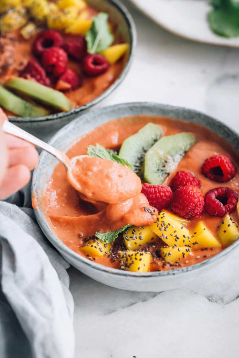 two grey bowls filled with tropical sweet potato smoothie bowl, topped with mango, kiwi, raspberries and mint