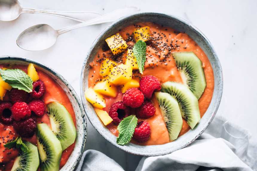 two grey bowls filled with tropical sweet potato sbreakfast bowl, topped with mango, kiwi, raspberries and mint