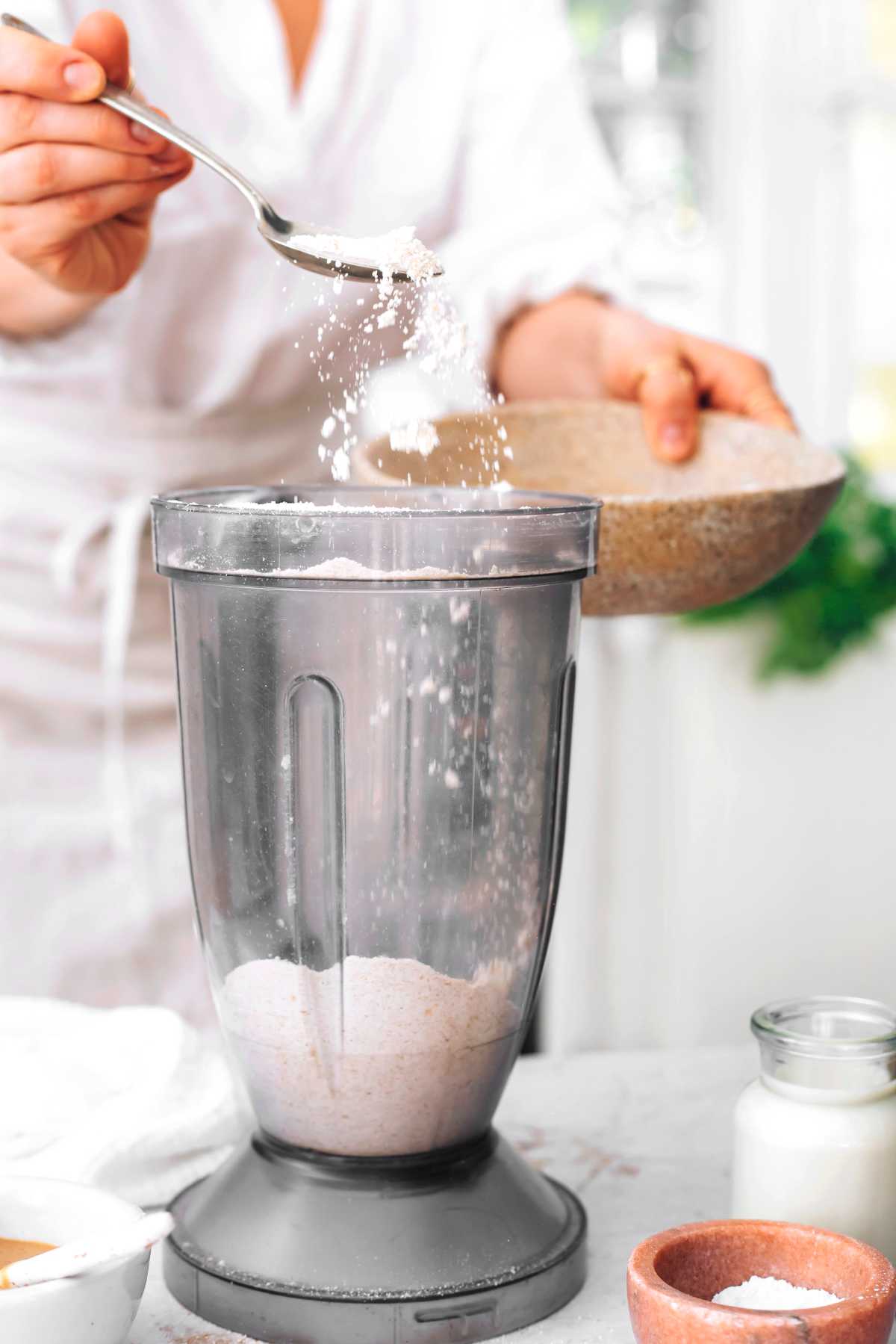 woman adding flour to a blender with a spoon