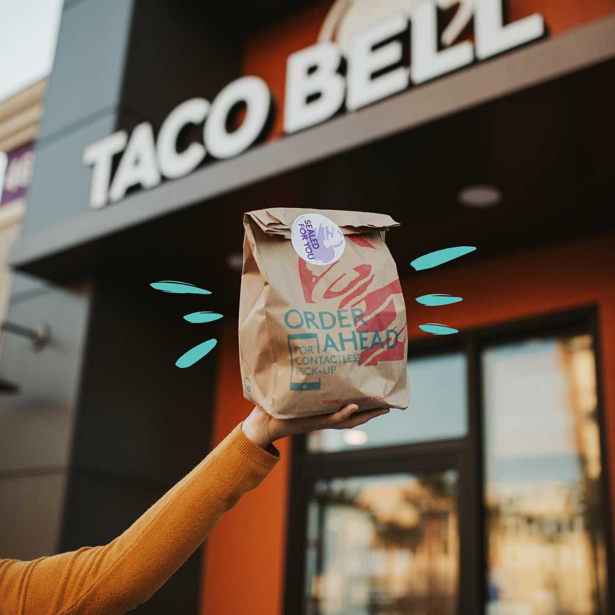 person holding a bag of vegan fast food in front of a Taco Bell
