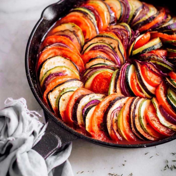 white table with cast iron skillet containing baked layered summer vegetables in tomato sauce