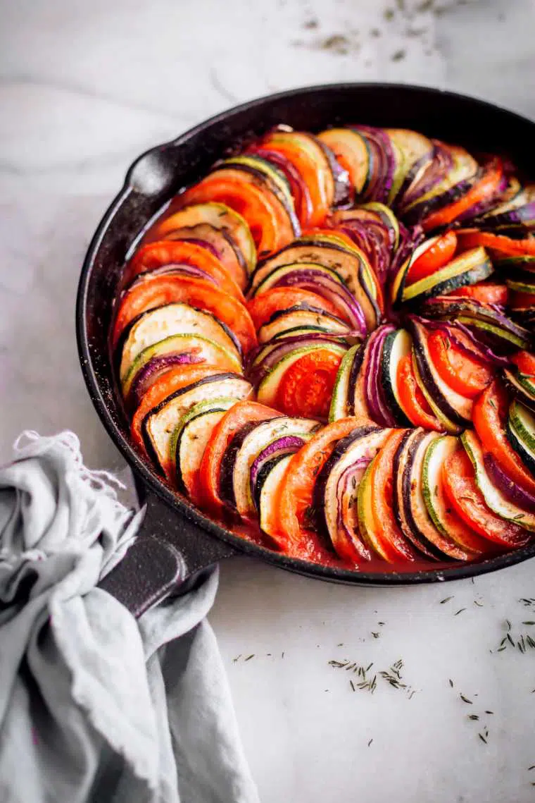 white table with cast iron skillet containing baked layered summer vegetables in tomato sauce