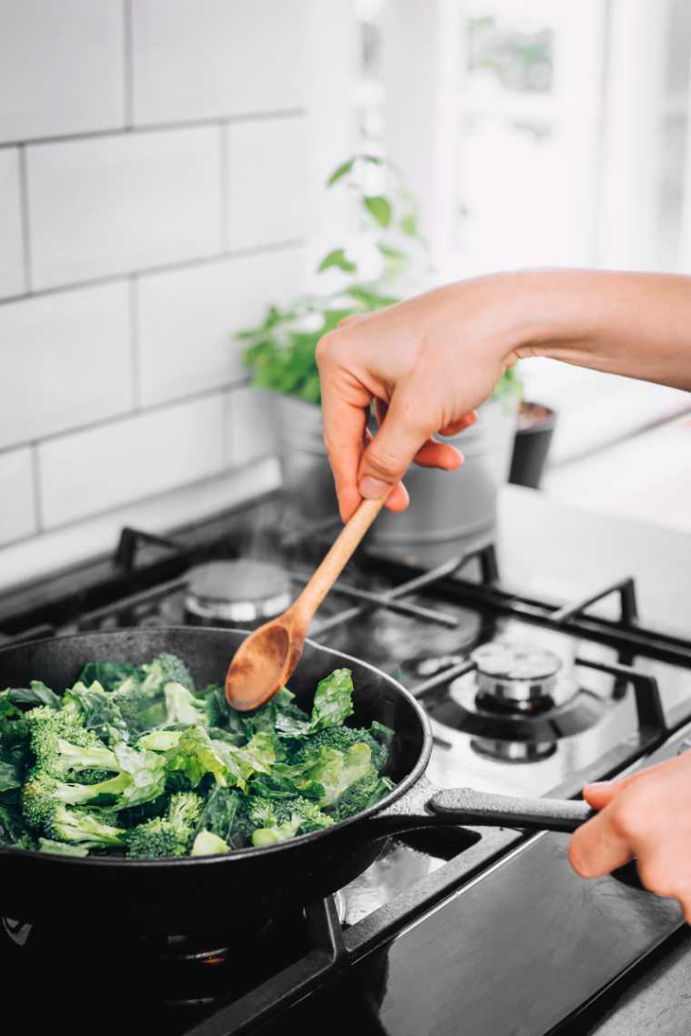 woman standing by a stove and sautéing green veggies in a pan