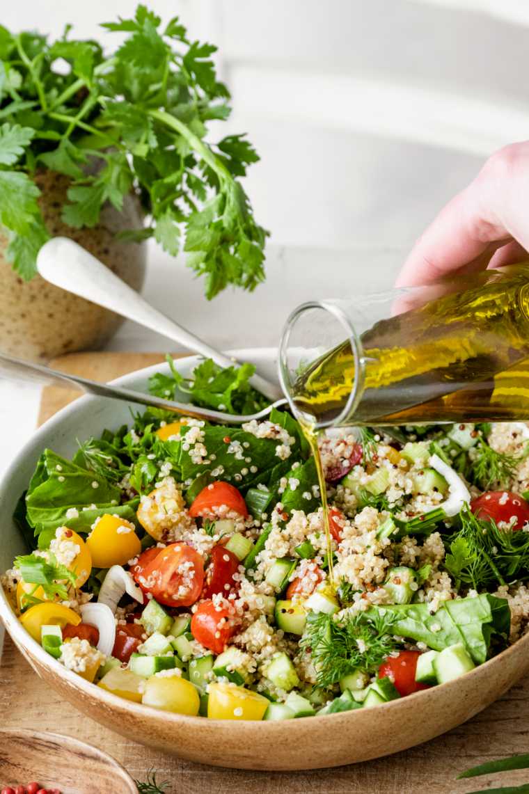 bowl of salad with quinoa being topped with olive oil