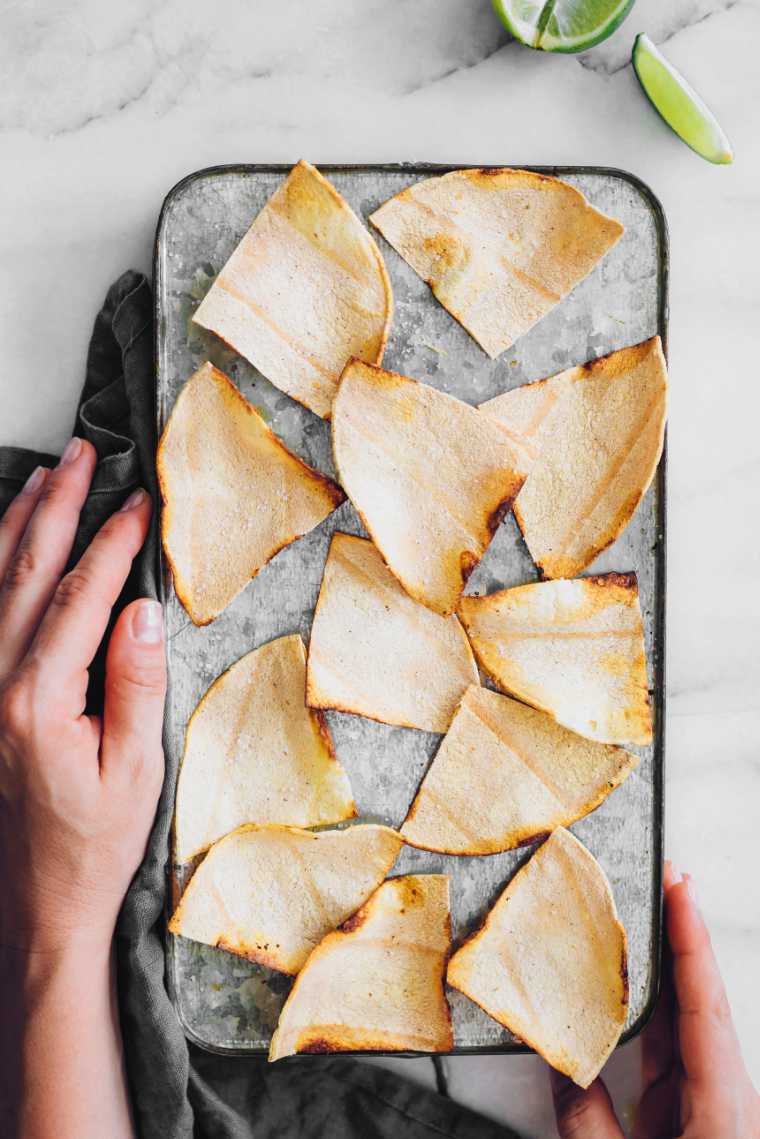 baking sheet held by two hands with freshly baked oil-free tortilla chips