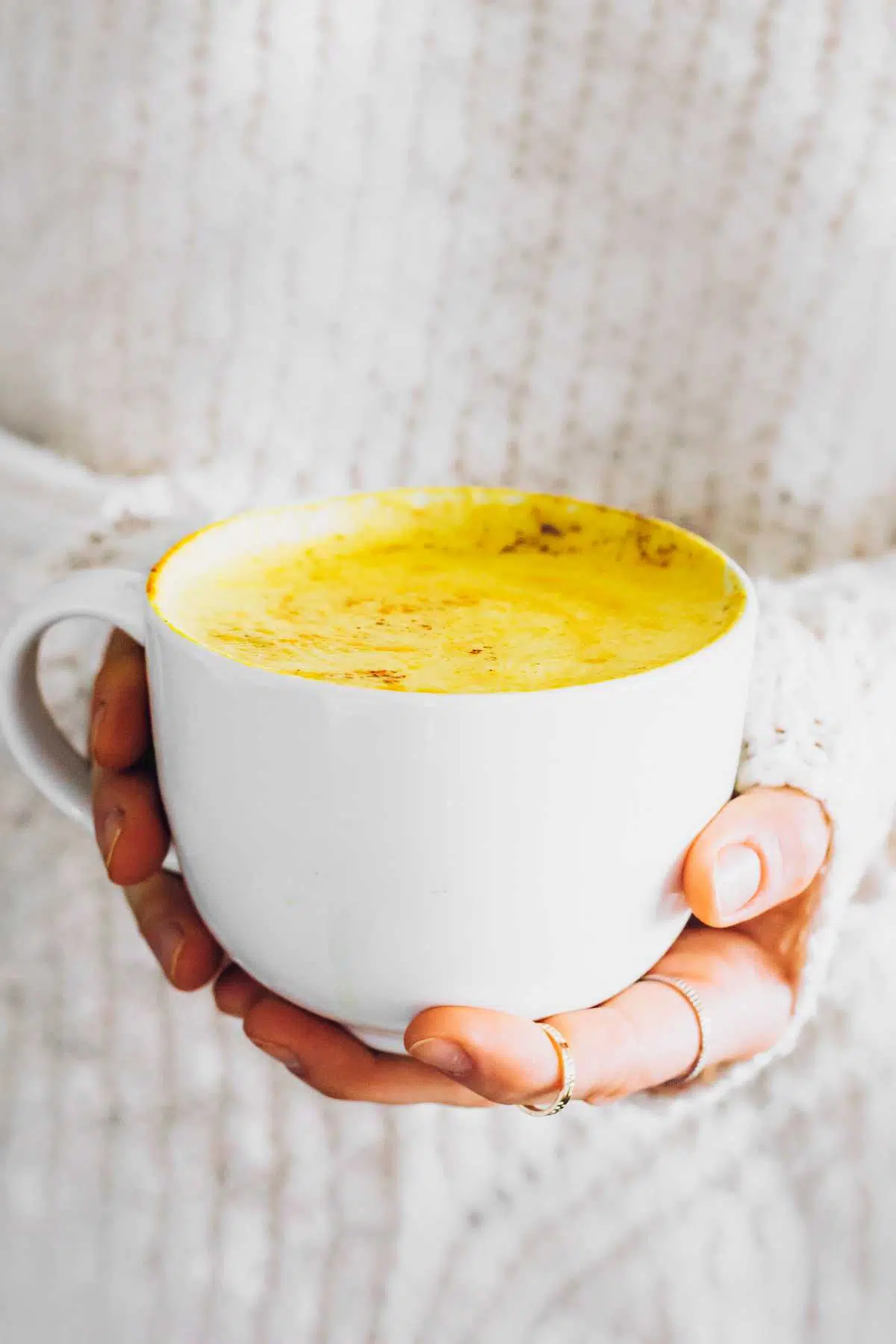 woman in sweater holding a Turmeric Latte in her hand