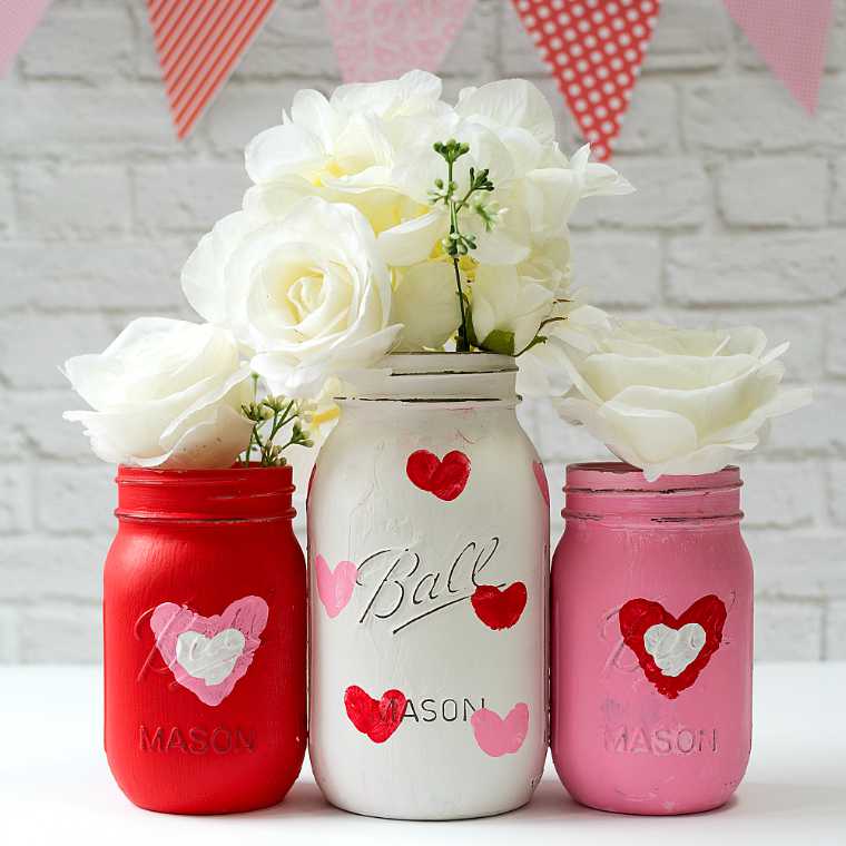 three different sized and colored Mason Jars used as vases for white roses