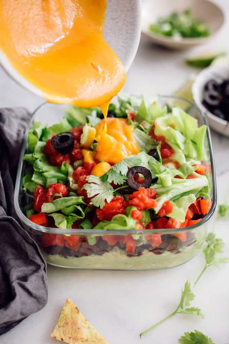 glass container with avocado, beans and fresh veggies on which vegan nacho cheese sauce is poured