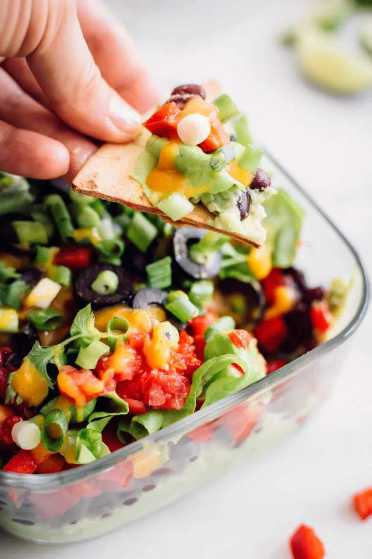 hand holding tortilla chip with some homemade seven layer dip