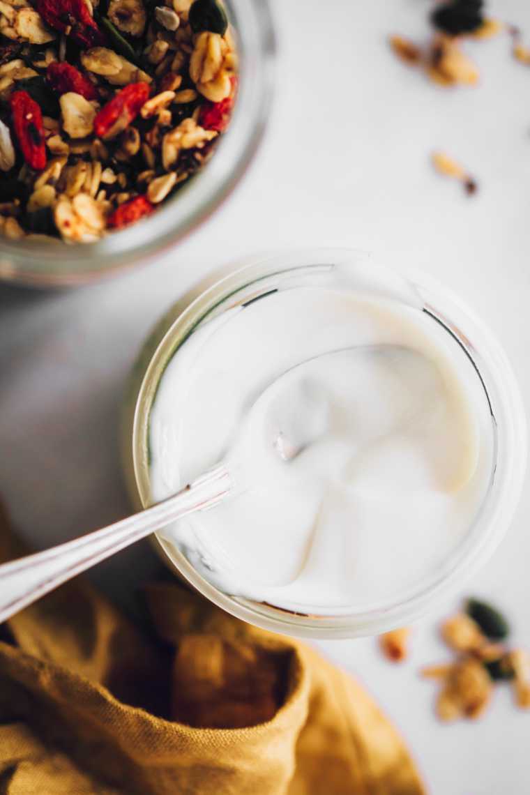 white table with some granola next to a jar of easy almond milk yogurt and a spoon