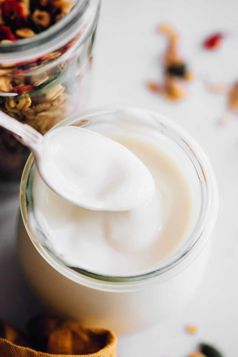 close up of a glass jar with dairy-free homemade almond yogurt being poured from a spoon