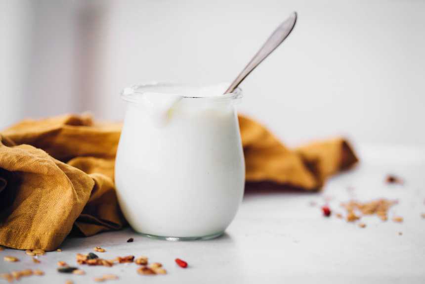 glass jar of creamy almond milk yogurt and a spoon on a white table