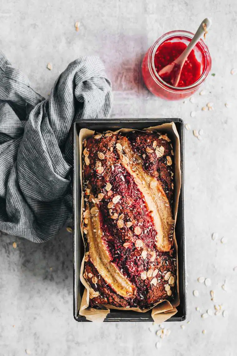 freshly baked raspberry banana bread on table next to raspberry jam