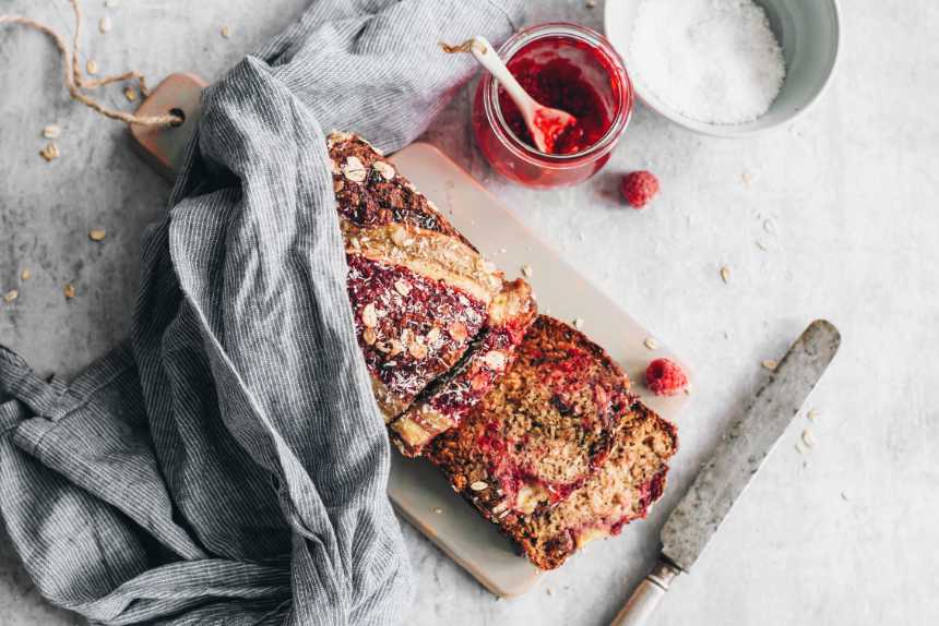 vegan sugar free raspberry banana bread under a towel on a chopping board next to a knife and jam