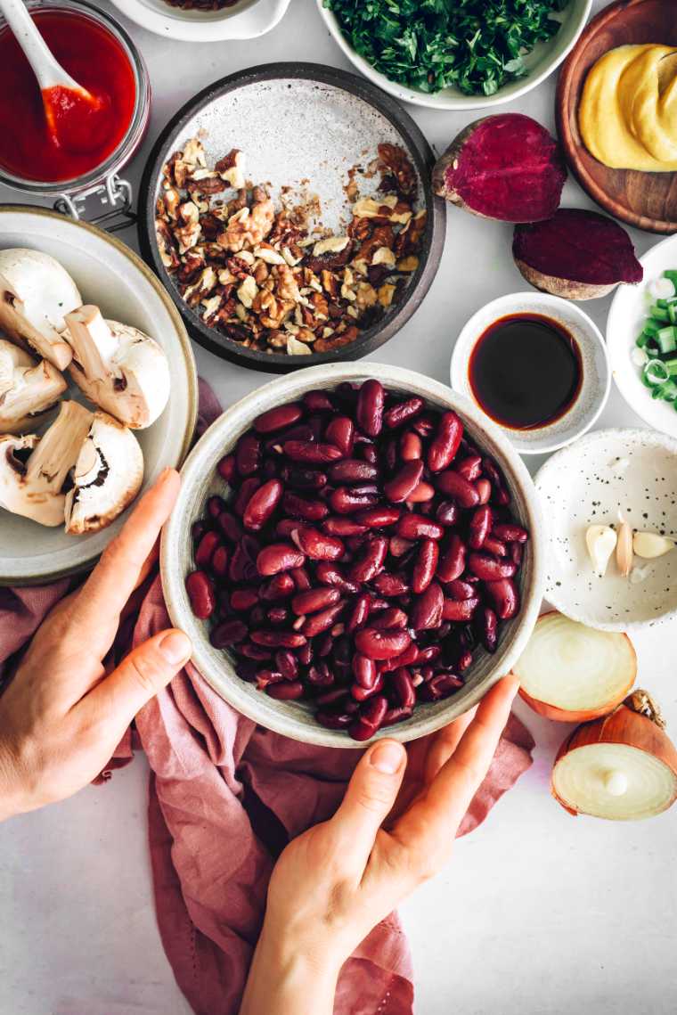 white table with different small bowls containing kidney beans, walnuts, mushrooms and herbs