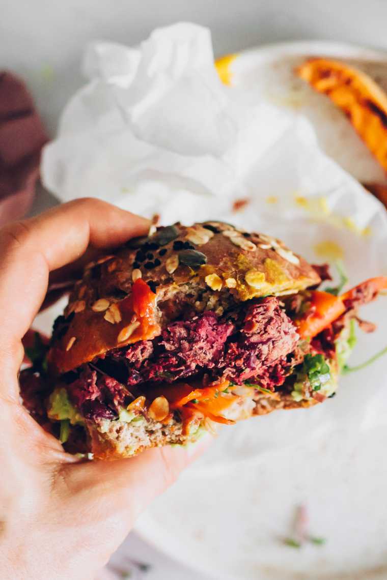 close up of purple beet burger in a hand with one bite taken out