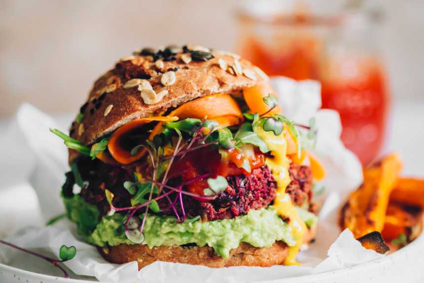 close up of colorful kidney bean beet burger in whole wheat bun with avocado, carrots and microgreens