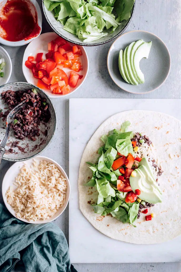 ingredients for vegan burrito, such as rice, bell peppers, avocado and beans, on a table