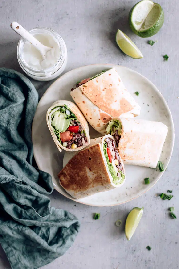 Finished vegan bean burrito cut into halves lying on plate