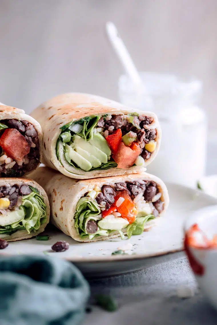 Close up of four colorful vegan burritos filled with avocado, rice and tomatoes
