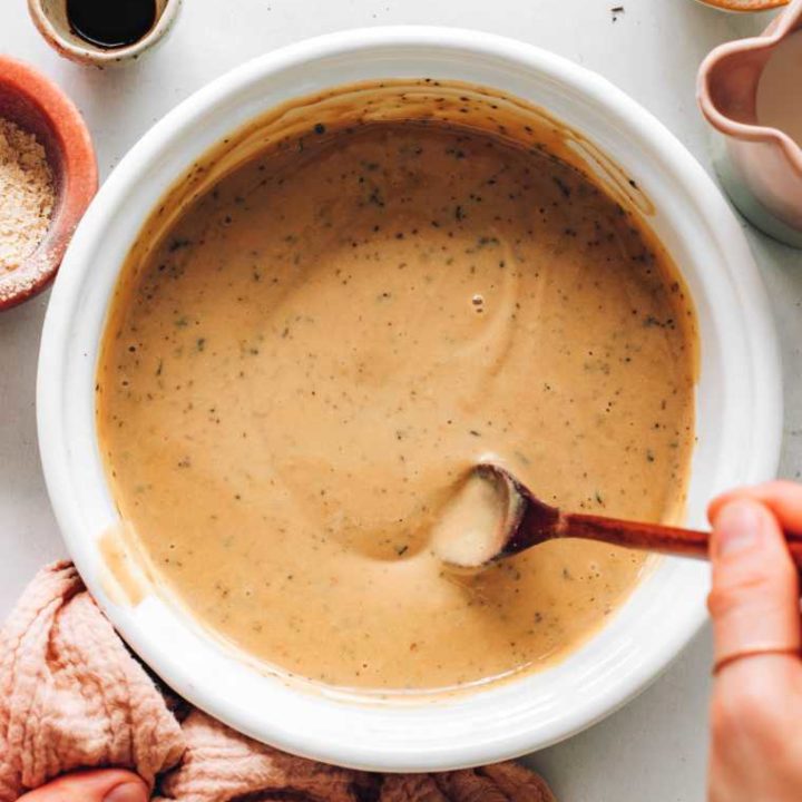 large white bowl with creamy vegan brown gravy that's being stirred with a spoon