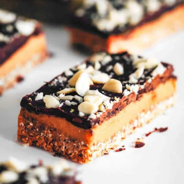 five no-bake vegan caramel slices with chocolate and almond topping on a white table