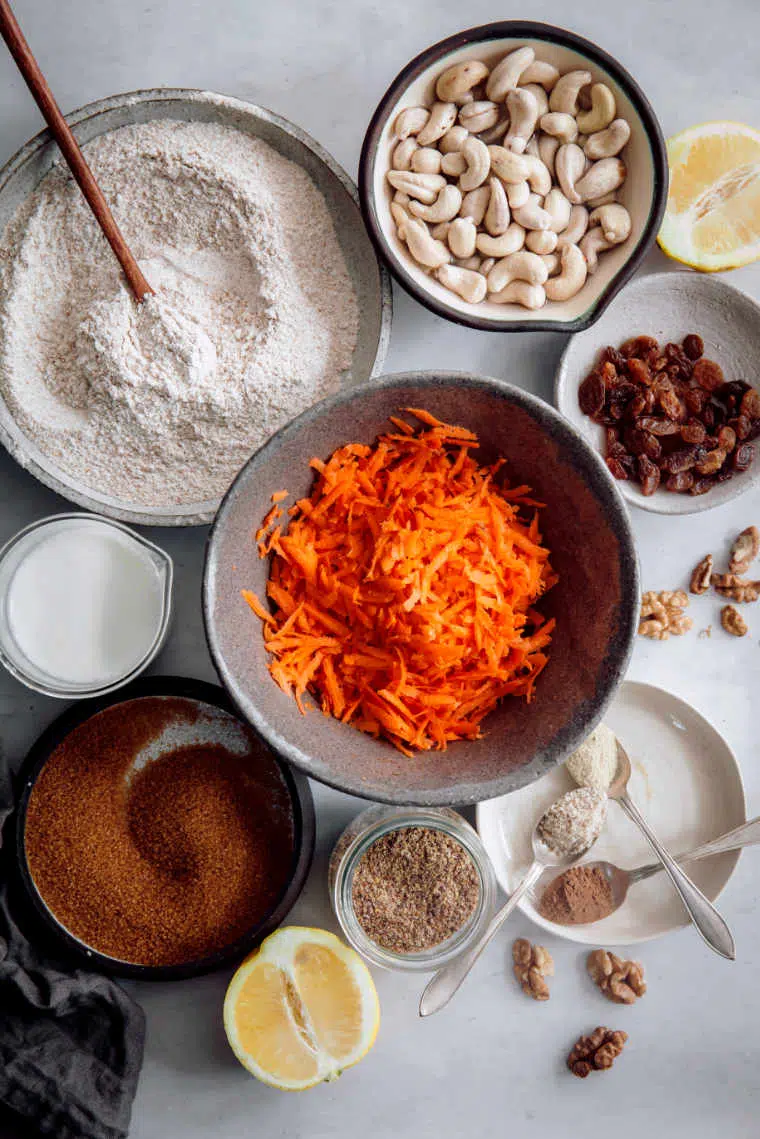 white table with different sized bowls containing carrots, whole wheat flour, applesauce, cashews and spices