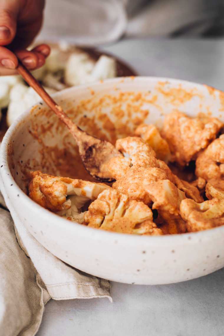 white bowl with spicy batter with which cauliflower bites are being coated with a wooden spoon