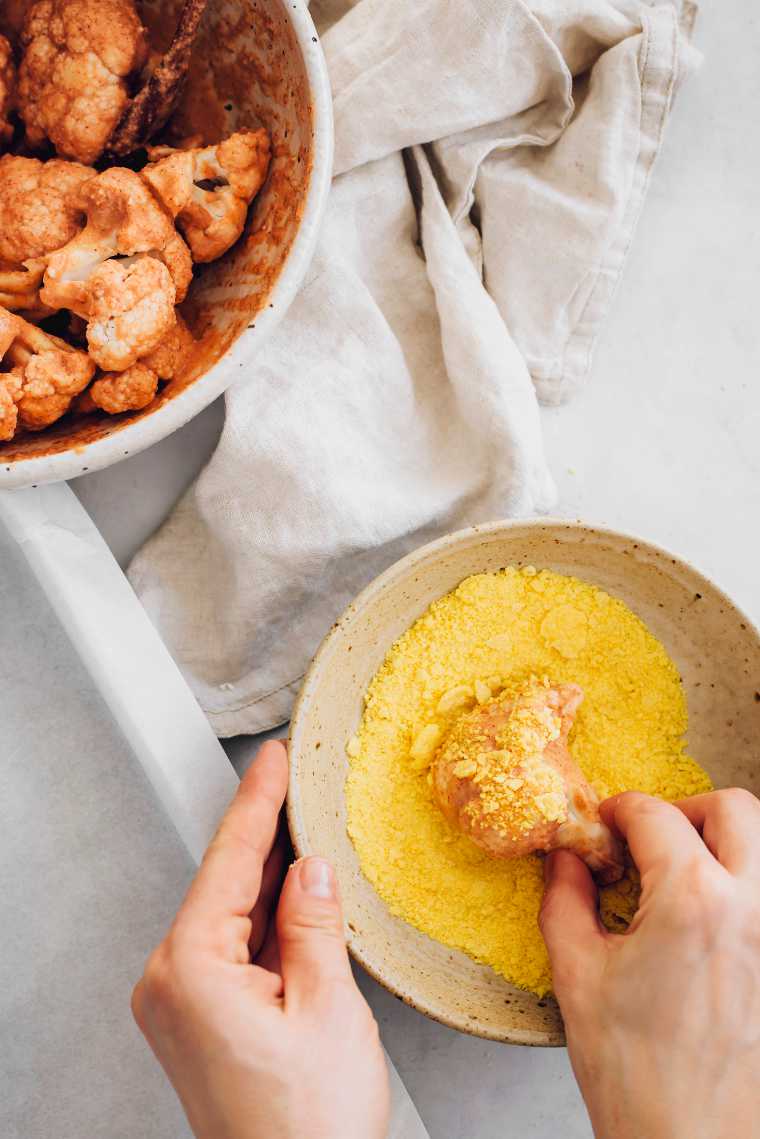 cauliflower florets with batter being coated with cornflakes crumbles in a small bowl