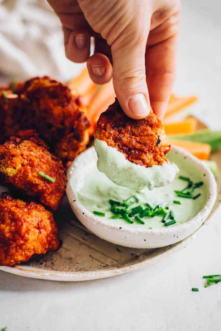 hand holding a baked cauliflower wing that's been dipped in some green vegan ranch